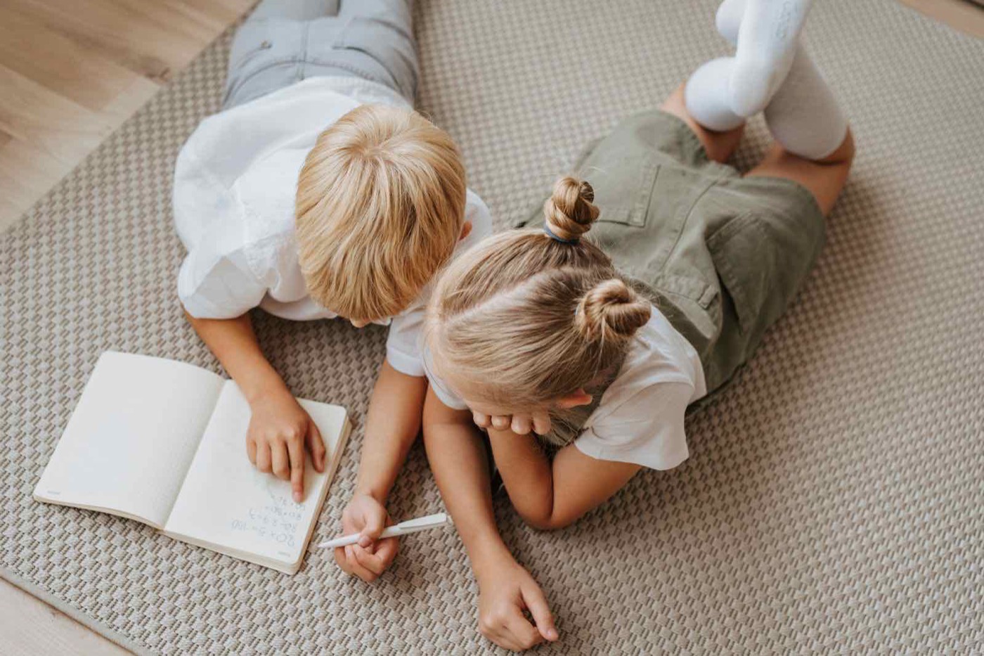 Two children lying on the floor working through a notebook together.